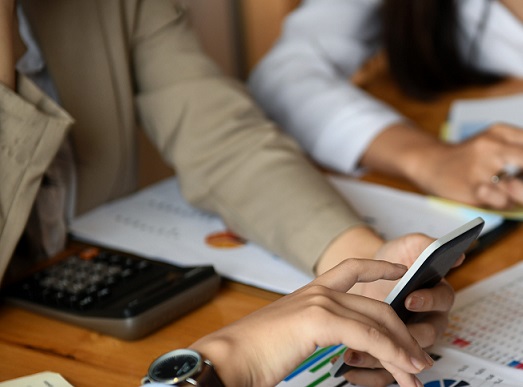 Staff team is planning an event to present customers. They are using smartphones and analyzing data graphs on the desk.